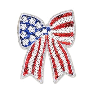 May include: A patriotic bow-shaped embellishment featuring the American flag design. The bow is adorned with red, white, and blue sequins, with a silver glitter outline. The bow is a decorative item.