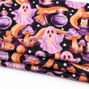 May include: A folded piece of fabric featuring a black background with a repeating pattern of light purple ghosts, orange butterflies, purple mushrooms, lit candles in purple holders, and purple potion bottles, all accented by small white stars.