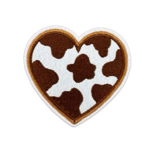 May include: A heart-shaped embroidered patch featuring a brown and white cow print pattern. The patch has a thick, stitched brown border and a thin white outer edge, creating a distinct outline for the heart shape against a plain background.