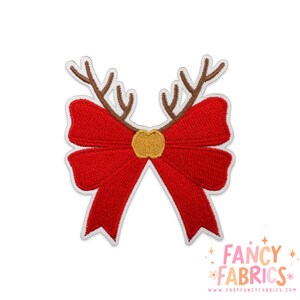 May include: A red embroidered patch shaped like a bow with brown reindeer antlers extending from the top. The center of the bow features a small, textured gold circle. The entire design is outlined in white thread against a plain background.
