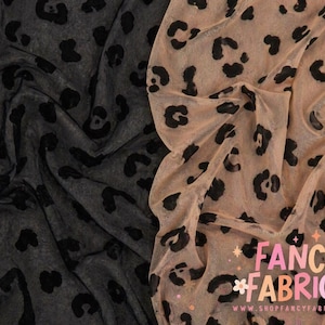 May include: Two fabric samples, one dark gray and one tan, both with a black leopard print pattern. The fabric is draped, showing the texture and design. The tan fabric has the text "FANCY FABRICS" in a colorful, stylized font.