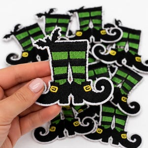 Può includere: Una collezione di toppe ricamate raffiguranti un paio di gambe con calze a righe verdi e nere e scarpe nere a punta ricurva con fibbie gialle. Ogni toppa è rifinita con un bordo bianco e un piccolo dettaglio a forma di pipistrello in alto.