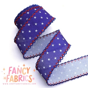 以下が含まれることがあります： 白い星と赤いジグザグトリムが付いた青いリボンのロール。Fancy Fabricsのリボンで、ウェブサイトのアドレスが表示されています。工芸品、装飾、ギフト包装に最適です。
