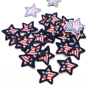 May include: A collection of star-shaped patches with a patriotic theme. Each patch features a navy blue border, red and white stripes, and white stars, resembling the American flag. The patches are scattered on a white surface.