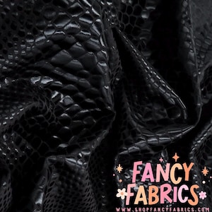 May include: Close-up of black fabric with a textured, reptile-like pattern. The material has a shiny, reflective surface. The words "Fancy Fabrics" are displayed in a colorful, stylized font.