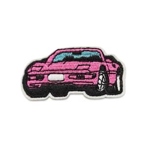 May include: An embroidered patch featuring a pink sports car with black outlines and detailing. The car has a light blue windshield, black tires, and a white rectangular license plate area. The entire design is bordered by a white edge.