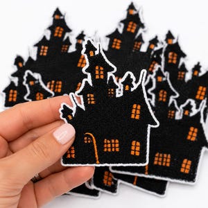 Puede incluir: Una colección de parches bordados con forma de casa encantada. Cada parche presenta una silueta negra de una casa de varios pisos con ventanas naranjas y un borde blanco. El diseño incluye una torre central alta y una puerta curva naranja.