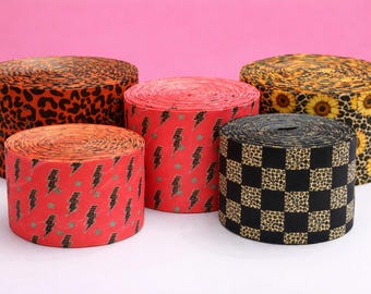 May include: Five rolls of decorative paper with various patterns. The patterns include leopard print, sunflowers, lightning bolts, and a checkered leopard print. The rolls are in shades of orange, red, yellow, and black.
