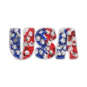 May include: A decorative USA sign with a patriotic design. The letters are embellished with red, white, and blue sequins, creating a sparkling effect. The letters are outlined with silver sequins.