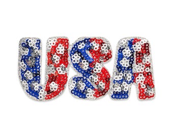 May include: A decorative USA sign with a patriotic design. The letters are embellished with red, white, and blue sequins, creating a sparkling effect. The letters are outlined with silver sequins.