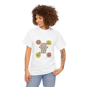 Peut inclure: Un t-shirt blanc avec un motif floral et le texte "LESS TALK. CREATE YOUR OWN LANE." Les fleurs sont dans des tons de marron et de vert. Le t-shirt est porté par une personne.