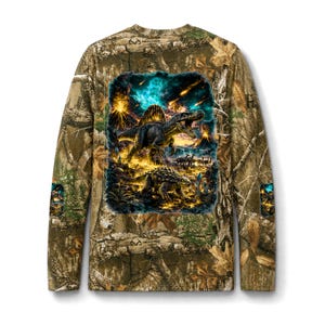 Peut inclure: Un t-shirt à manches longues avec un motif camouflage Realtree dans des tons marron, vert et beige. Le dos présente un graphique vibrant d'un Spinosaurus et d'un Ankylosaurus dans un paysage préhistorique avec des volcans et une pluie de météores.