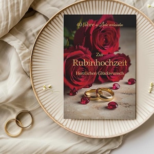 Könnte beinhalten: Eine Grußkarte mit roten Rosen und goldenen Ringen, die einen 40. Hochzeitstag feiert. Der Text ist auf Deutsch. Die Karte liegt auf einem dekorativen Teller.