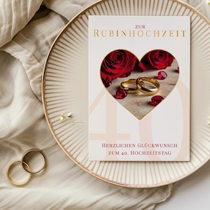 Könnte beinhalten: Eine Grußkarte zum 40. Hochzeitstag mit einem herzförmigen Ausschnitt, der rote Rosen und goldene Ringe zeigt. Die Karte liegt auf einem dekorativen Teller, mit goldenem Text.