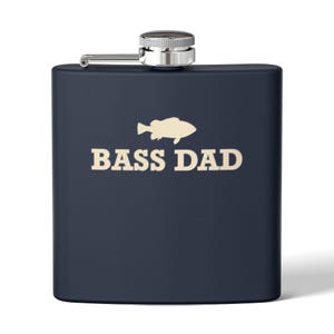 Könnte beinhalten: Ein matter, marineblauer Metallflachmann mit silberfarbenem Schraubverschluss. Auf der Vorderseite befindet sich eine cremefarbene Grafik der Silhouette eines Fisches über dem Text BASS DAD in einer fetten, serifenlosen Großbuchstabenschrift.