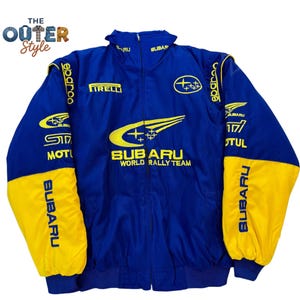 May include: Blue and yellow Subaru World Rally Team jacket. The jacket features the Subaru logo, sponsor logos, and text. The sleeves are yellow with blue cuffs. The jacket has a full zipper and a stand-up collar.
