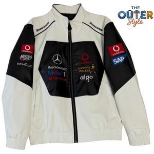 May include: White and black racing jacket with multiple sponsor logos, including Vodafone, Mercedes-Benz, and Bridgestone. The jacket has a full zipper and a stand-up collar. The text "THE OUTER Style" is visible.