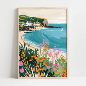 Könnte beinhalten: Ein gerahmter Kunstdruck, der eine Küstenlandschaft darstellt. Das Kunstwerk zeigt einen Strand mit türkisfarbenem Wasser, weiße Gebäude auf einer grünen Klippe und bunte Blumen im Vordergrund. Ein Segelboot ist in der Ferne zu sehen.