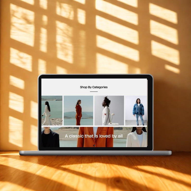May include: A laptop displaying a website with the text "Shop By Categories" and the phrase "A classic that is loved by all." The website showcases images of clothing. The laptop is on a wooden surface with sunlight and shadows.