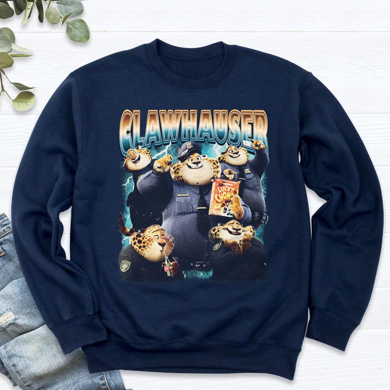 Puede incluir: Sudadera azul marino con un dise&ntilde;o de Clawhauser de Zootopia. El dise&ntilde;o muestra a Clawhauser con uniforme de polic&iacute;a, sosteniendo una bolsa de Lucky Chomps. La palabra "CLAWHAUSER" est&aacute; impresa encima de los personajes.