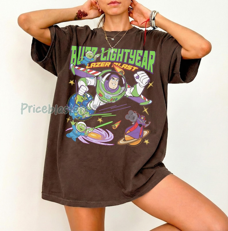 May include: Brown t-shirt featuring a graphic of Buzz Lightyear in a space scene with the text "Buzz Lightyear Lazer Blast". The design includes planets, stars, and other characters from the movie.