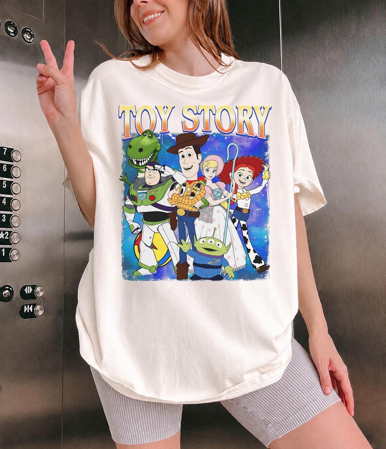 Puede incluir: Camiseta color crema con un gr&aacute;fico de personajes de la pel&iacute;cula animada "Toy Story". El dise&ntilde;o incluye a Woody, Buzz Lightyear, Jessie y otros personajes. Las palabras "TOY STORY" est&aacute;n impresas en la parte superior en naranja y azul.