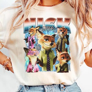 Pode incluir: Camiseta creme com um gr&aacute;fico de Nick Wilde de Zootopia. O design inclui v&aacute;rias imagens de Nick em v&aacute;rias roupas, com o nome "Nick Wilde" em uma fonte retr&ocirc;. A camiseta &eacute; uma pe&ccedil;a de roupa casual.