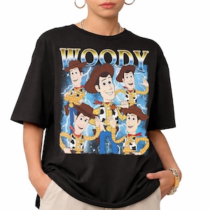 May include: Black t-shirt featuring a graphic of Woody from Toy Story. The design includes multiple images of Woody with a blue lightning background and the word "WOODY" in gold and blue lettering.