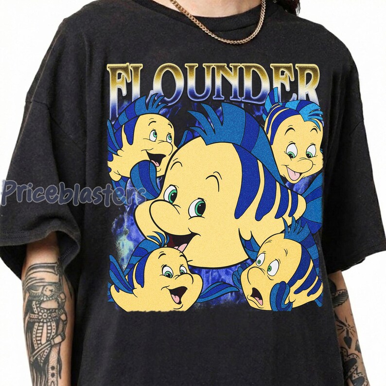 May include: Dark gray t-shirt featuring a graphic of Flounder from The Little Mermaid. The design includes multiple yellow and blue fish with the word "FLOUNDER" in gold lettering. The shirt has a vintage, distressed look.