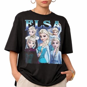 May include: Black t-shirt featuring a graphic of Elsa from the movie Frozen. The graphic includes multiple images of Elsa with the word "ELSA" in blue text. The t-shirt is a short-sleeved, crew neck style.