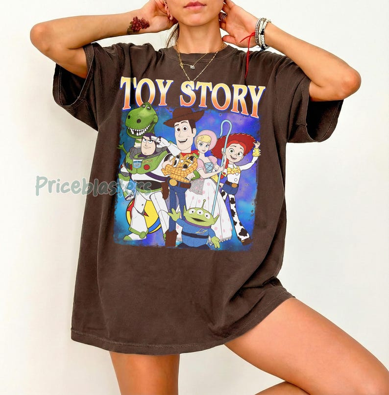 Puede incluir: Una camiseta marr&oacute;n con la inscripci&oacute;n "TOY STORY" en letras amarillas y naranjas. El gr&aacute;fico representa a los personajes de la pel&iacute;cula de animaci&oacute;n, incluyendo a Woody, Buzz Lightyear y Rex, sobre un fondo azul y morado.
