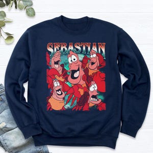 Pu&ograve; includere: Felpa blu navy con una grafica di Sebastian il granchio de La Sirenetta. Il design include pi&ugrave; immagini di Sebastian con la scritta "Sebastian" sopra. La felpa &egrave; uno stile girocollo.