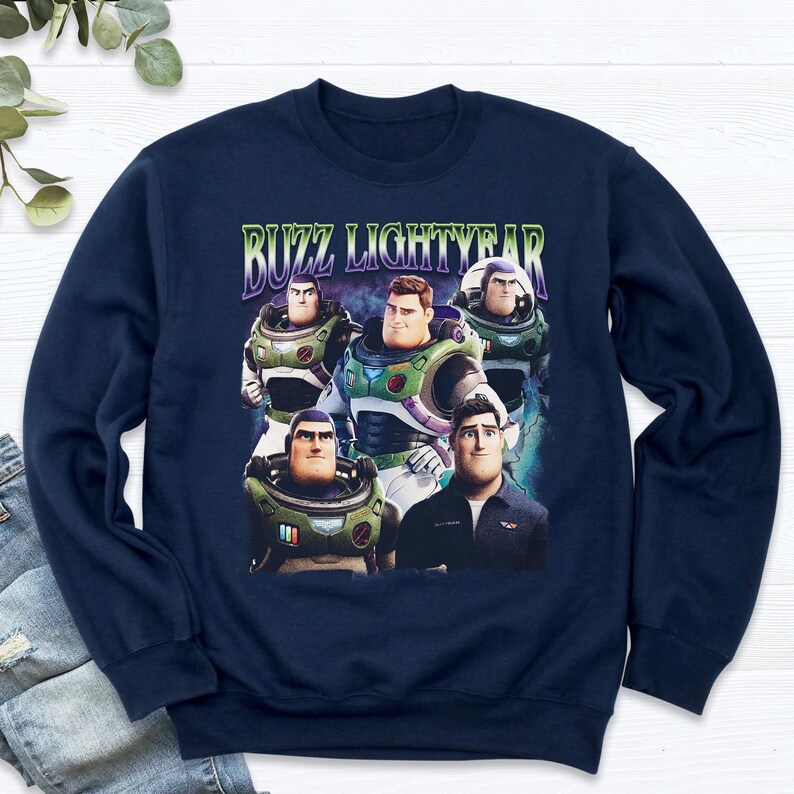 May include: Navy blue sweatshirt featuring a graphic of Buzz Lightyear and the text "BUZZ LIGHTYEAR" in green and purple. The graphic shows multiple images of Buzz Lightyear in various poses. The sweatshirt is made of a soft material.