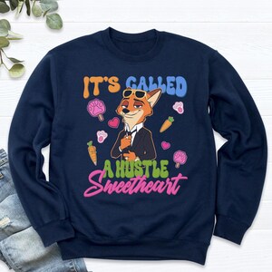 May include: Navy blue sweatshirt with a cartoon fox wearing sunglasses and a suit. The text "IT'S CALLED A HUSTLE Sweetheart" is printed on the front, along with paw prints, carrots, and lollipops.