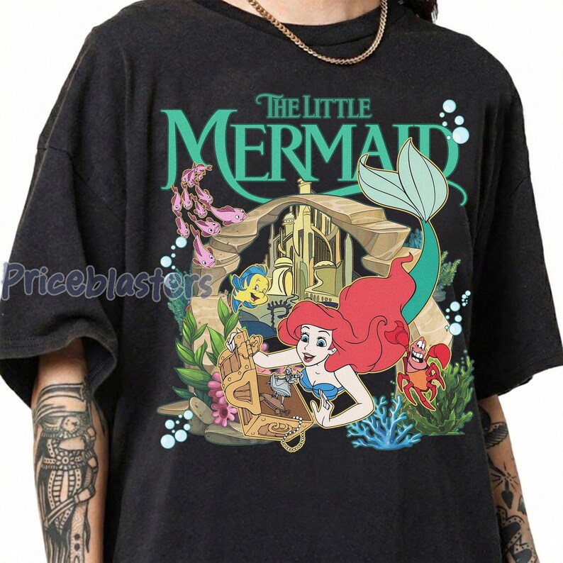 Może przedstawiać: Czarny t-shirt z kolorową grafiką Arielki z Małej Syrenki. Projekt zawiera napis "The Little Mermaid", Ariel, Florka, Sebastiana i skrzynię skarb&oacute;w. Koszulka ma okrągły dekolt i kr&oacute;tkie rękawy.