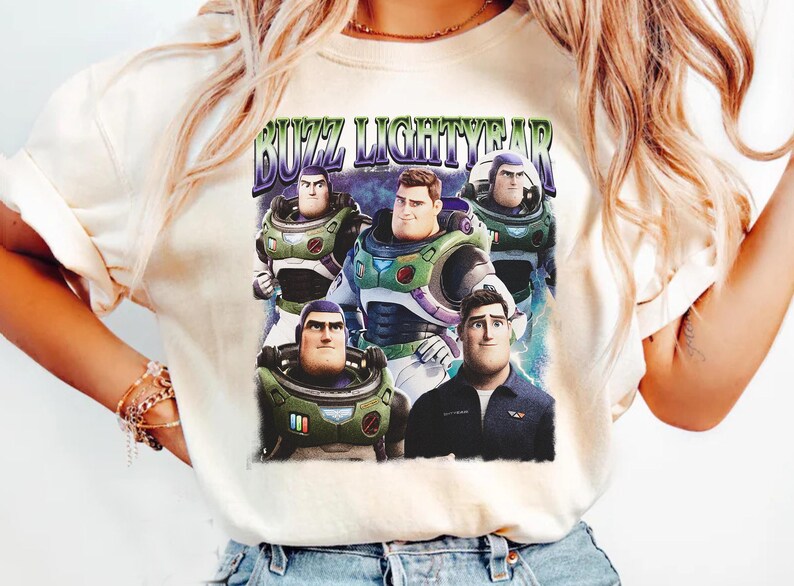 May include: Cream-colored t-shirt featuring a graphic of Buzz Lightyear from Toy Story. The design includes multiple images of Buzz in his spacesuit and the text "BUZZ LIGHTYEAR" in a retro font. The shirt is a casual wear item.