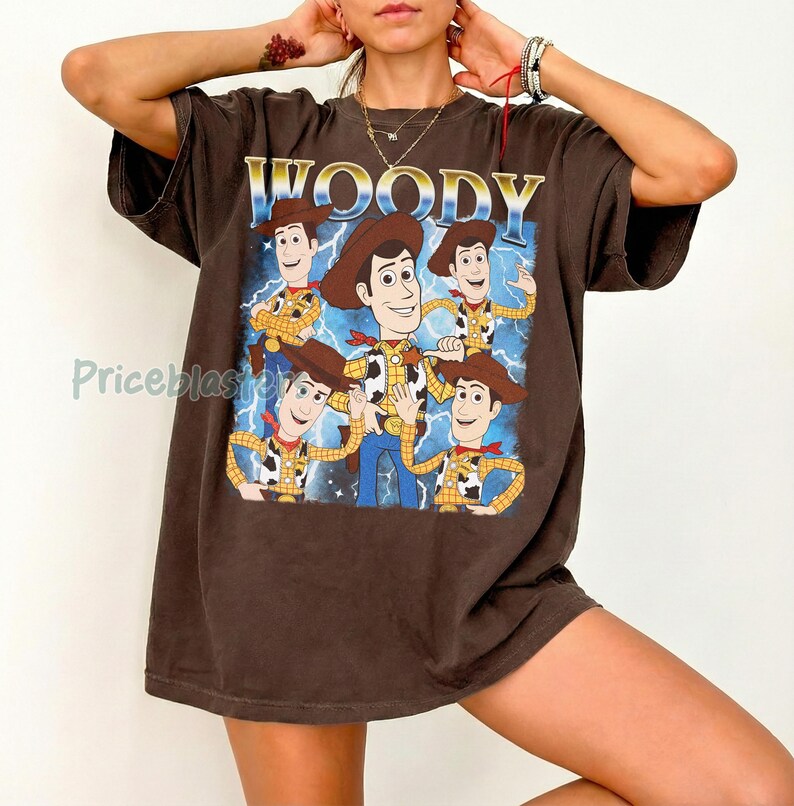 May include: Brown t-shirt featuring a graphic of Woody from Toy Story. The design includes the word "WOODY" in gold lettering above a cartoon image of Woody with a blue lightning background. The shirt has short sleeves.