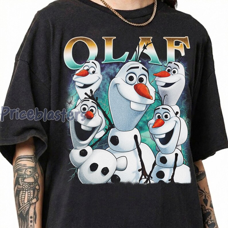 Puede incluir: Camiseta gris oscuro con un gr&aacute;fico de Olaf de Frozen. El dise&ntilde;o incluye m&uacute;ltiples personajes de Olaf con narices de zanahoria y caras sonrientes. La palabra "OLAF" est&aacute; impresa en la parte superior en una fuente colorida.