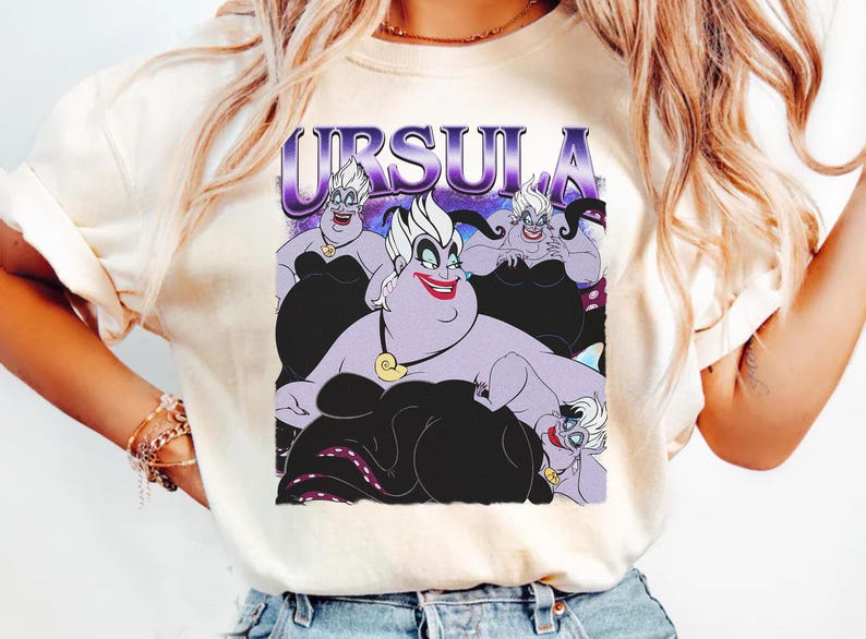 May include: Cream-colored t-shirt featuring a graphic of Ursula from The Little Mermaid. The design includes the word "URSULA" in purple and images of Ursula in various poses, with black and purple accents.