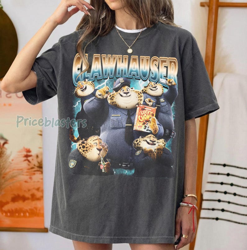 Puede incluir: Camiseta gris oscuro con un dise&ntilde;o de Clawhauser de Zootr&oacute;polis. El dise&ntilde;o incluye a Clawhauser con uniforme de polic&iacute;a, sosteniendo una bolsa de Lucky Chom, y la palabra "Clawhauser". La camiseta tiene un aspecto vintage.