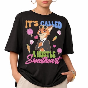 May include: Black t-shirt with a cartoon fox wearing sunglasses and a suit. The shirt has the text "IT'S CALLED A HUSTLE Sweetheart" in colorful bubble letters, along with cartoon paw prints, carrots, and hearts.