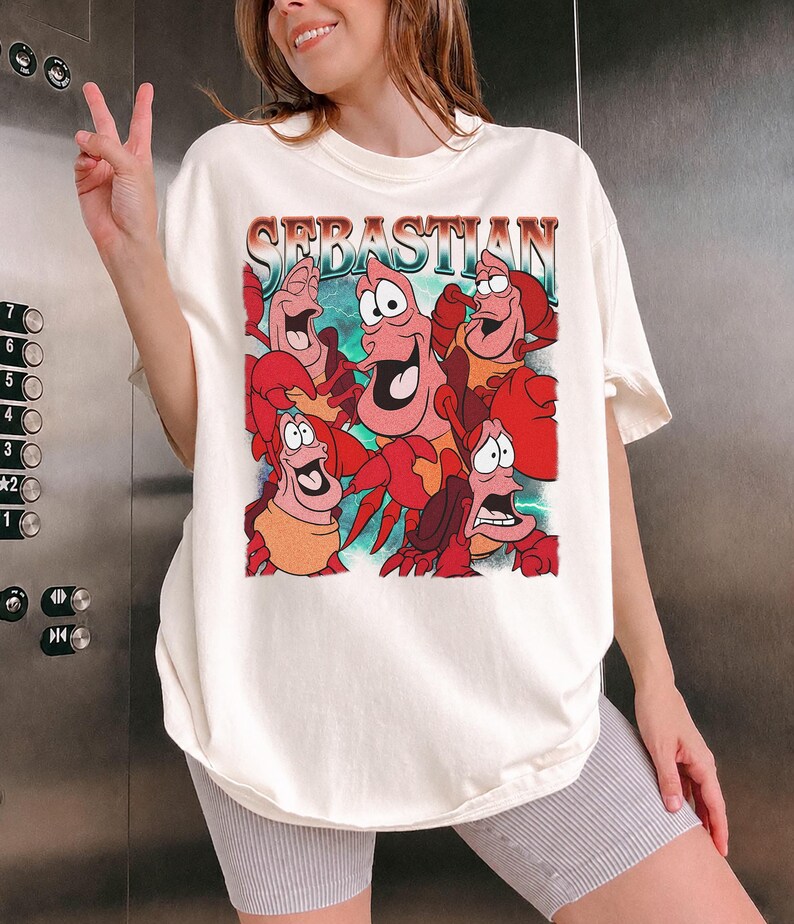 Pu&ograve; includere: T-shirt color crema con una grafica del personaggio Sebastian de La Sirenetta. Il design include la parola "Sebastian" in un font retr&ograve;, con diversi granchi dei cartoni animati in varie pose. La maglietta &egrave; di vestibilit&agrave; ampia.