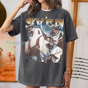 May include: Dark gray t-shirt featuring a graphic of four reindeer with the word "SVEN" in gold and blue. The reindeer have brown and white fur, and some have antlers. The shirt has a vintage, worn look.