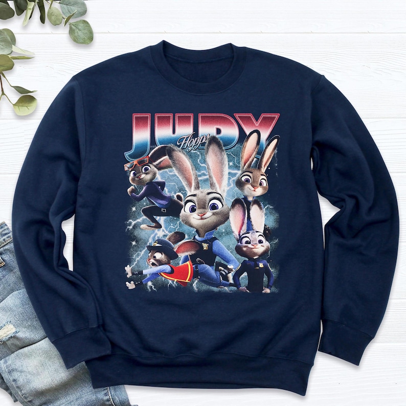 Op de afbeelding: Marineblauwe sweatshirt met een afbeelding van Judy Hopps uit Zootopia. Het ontwerp toont Judy en andere personages met de tekst "JUDY Hopps" in een rode, witte en blauwe letter. De sweatshirt is gemaakt van zacht materiaal.