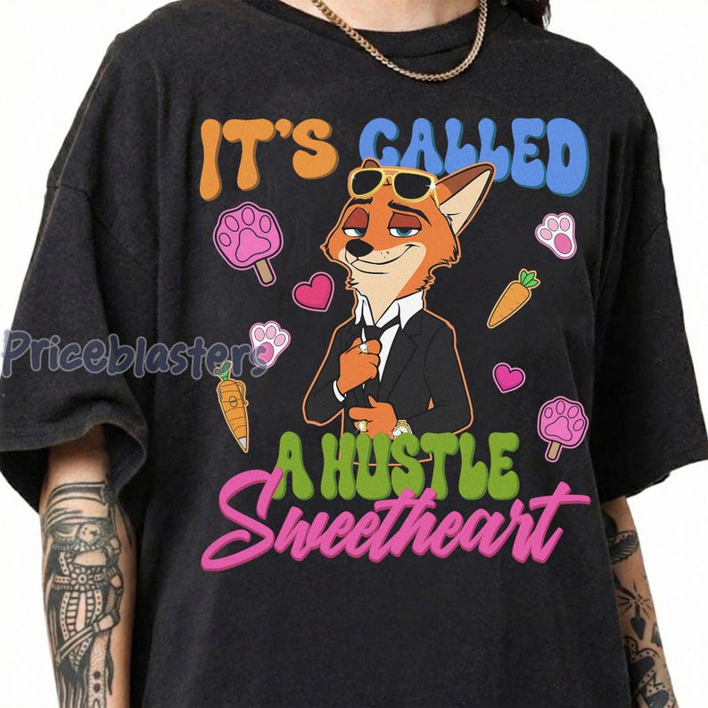 May include: Dark gray t-shirt featuring a cartoon fox in a suit with sunglasses. The shirt has the text "IT'S CALLED A HUSTLE Sweetheart" in orange, blue, and pink. Pink paw prints, hearts, and carrots surround the fox.