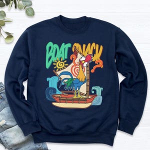 Puede incluir: Sudadera azul marino con un gallo de dibujos animados en un barco y el texto "BOAT SNACK". El dise&ntilde;o incluye un sol, olas y un signo de interrogaci&oacute;n. El gallo tiene plumas rojas, amarillas y azules.