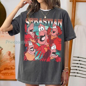 Pu&ograve; includere: T-shirt grigio scuro con una grafica colorata del personaggio Sebastian de La Sirenetta. La parola "SEBASTIAN" &egrave; stampata sopra la grafica in un font retr&ograve;. La maglietta ha una vestibilit&agrave; ampia.