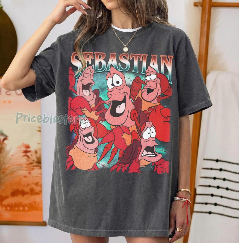 Pu&ograve; includere: T-shirt grigio scuro con una grafica colorata del personaggio Sebastian de La Sirenetta. La parola "SEBASTIAN" &egrave; stampata sopra la grafica in un font retr&ograve;. La maglietta ha una vestibilit&agrave; ampia.