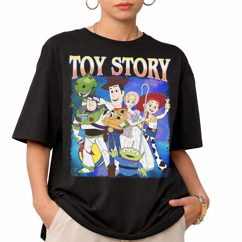 Puede incluir: Camiseta negra con un gr&aacute;fico de personajes de la pel&iacute;cula animada "Toy Story". El dise&ntilde;o incluye a Woody, Buzz Lightyear, Jessie y otros personajes, con las palabras "TOY STORY" en la parte superior en una fuente retro.