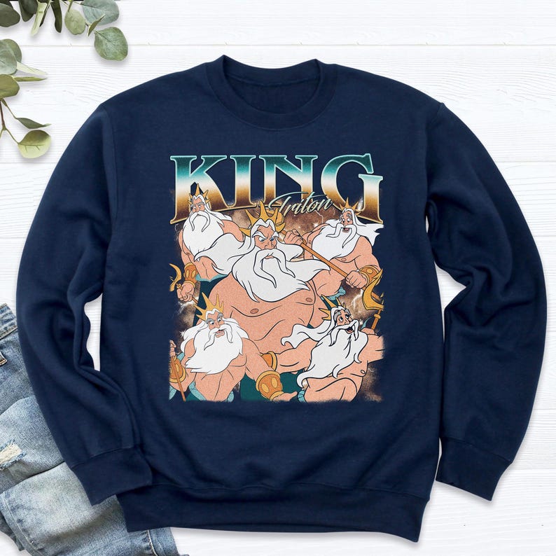 May include: Navy blue sweatshirt featuring a graphic of King Triton from The Little Mermaid. The design includes the text "KING Triton" in a vintage style font, with multiple images of the character. The sweatshirt is a crew neck style.
